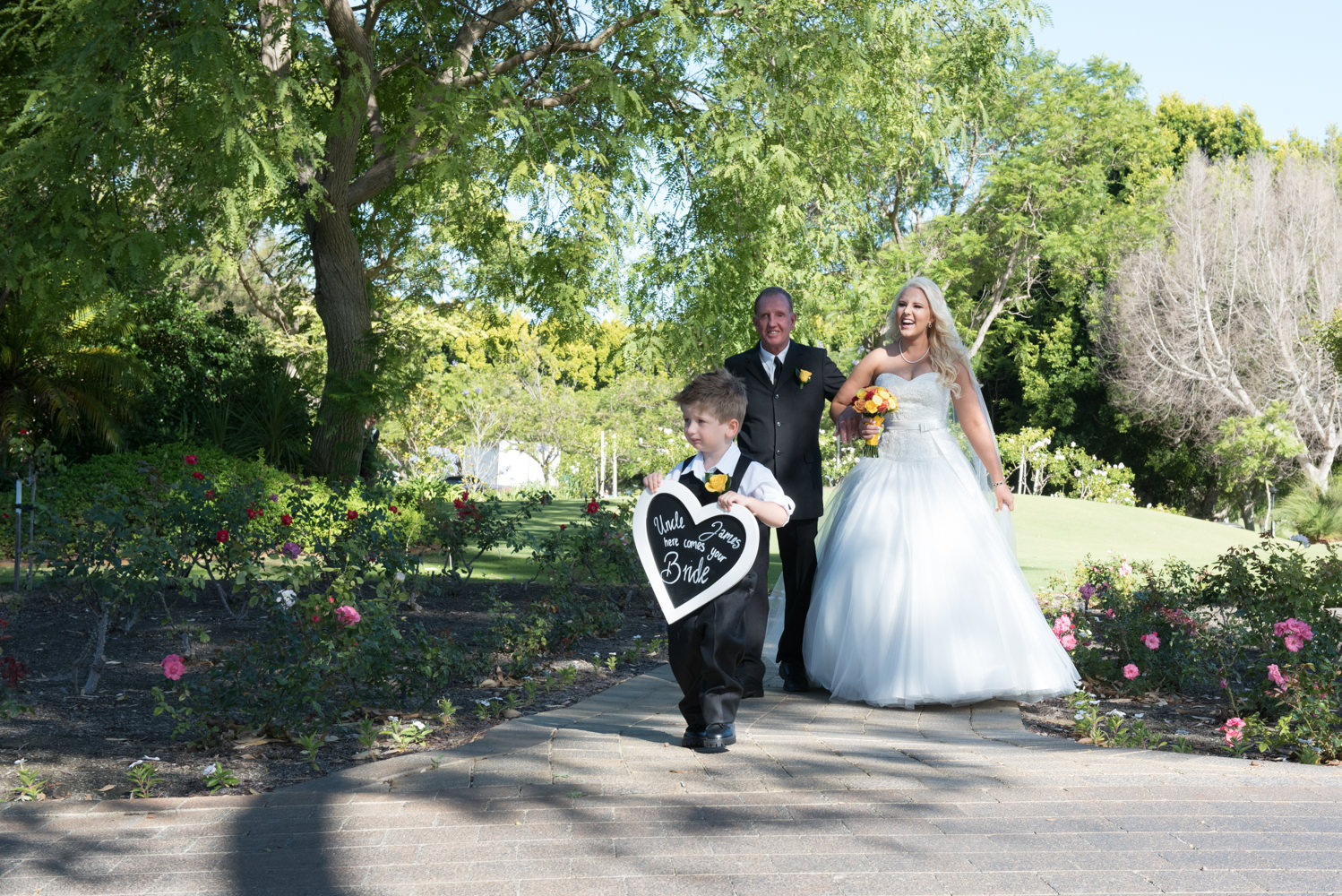 Page boy holds heart shaped Here comes the Bride sign when walking down the aisle