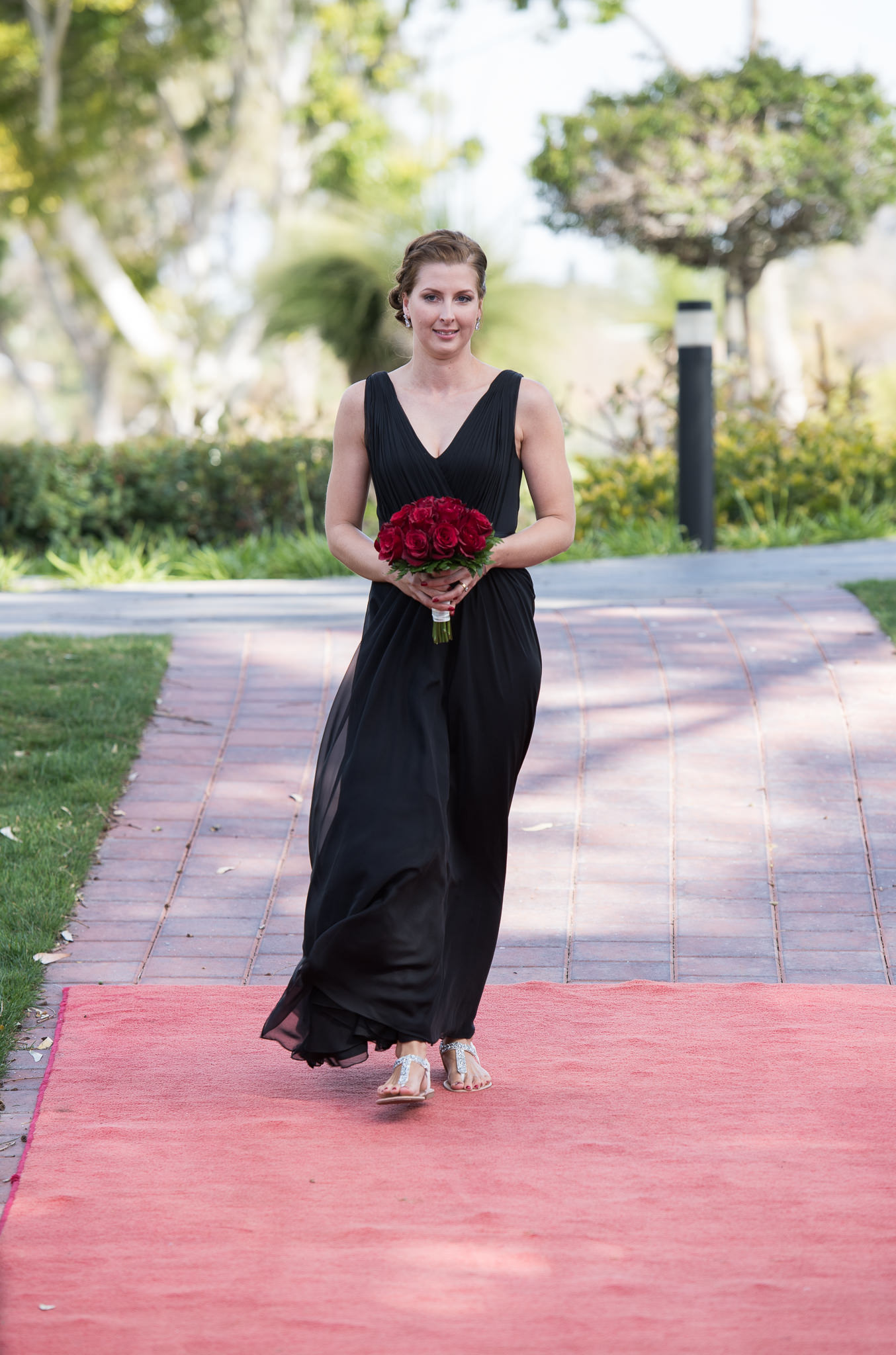 bridesmaid walks down the red carpet aisle with red rose bouquet