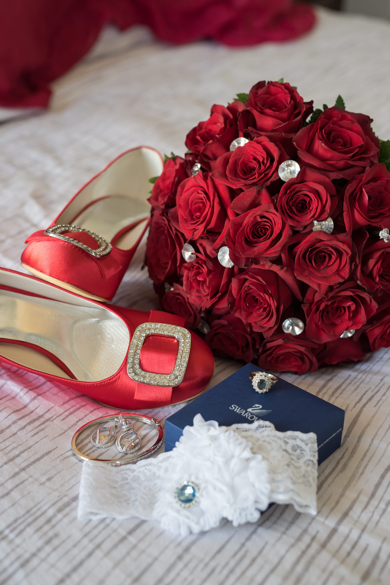 bridal shoes, jewellery, garter and bouquet arranged on a bed