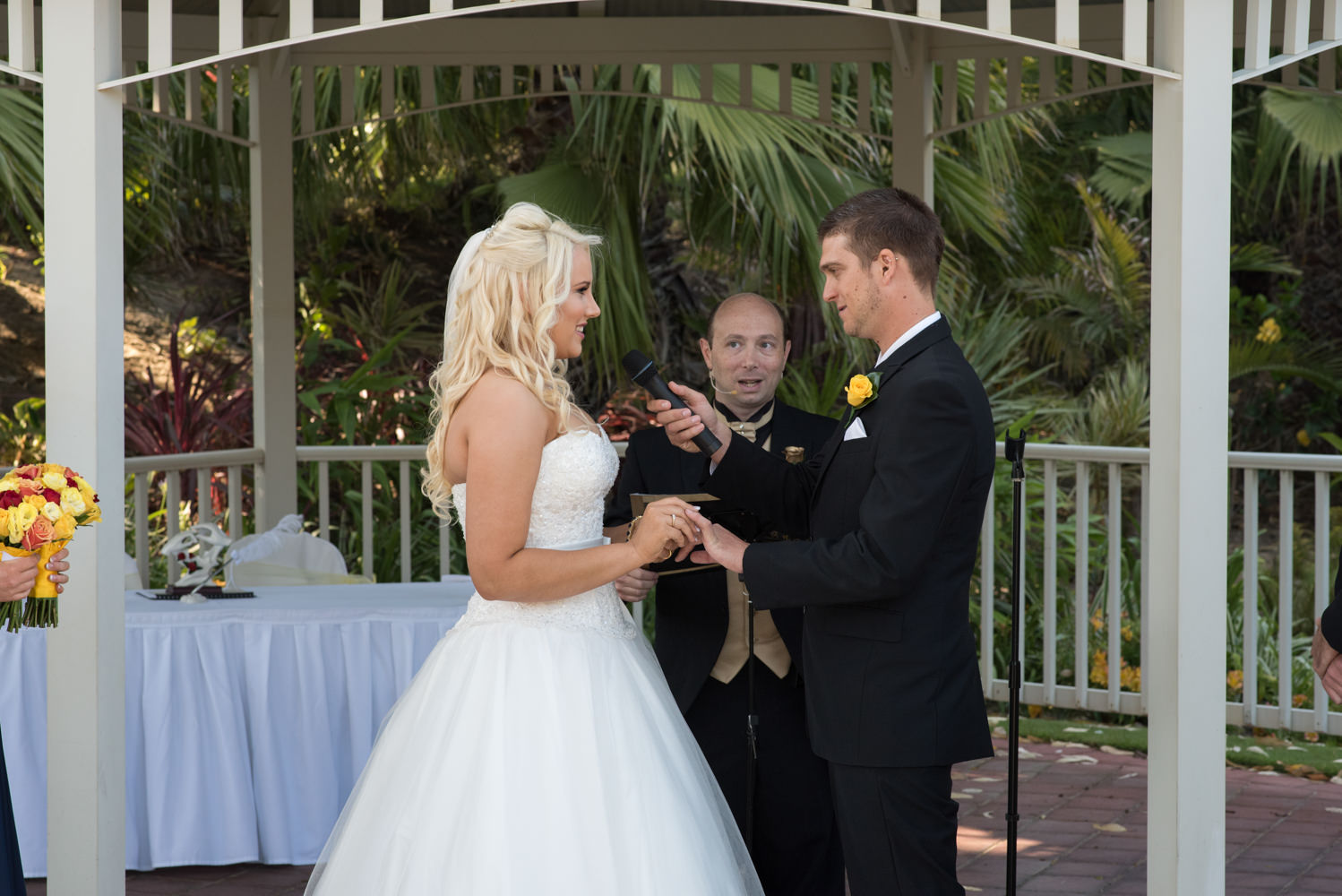 Bride puts ring on grooms hand with celebrant behind