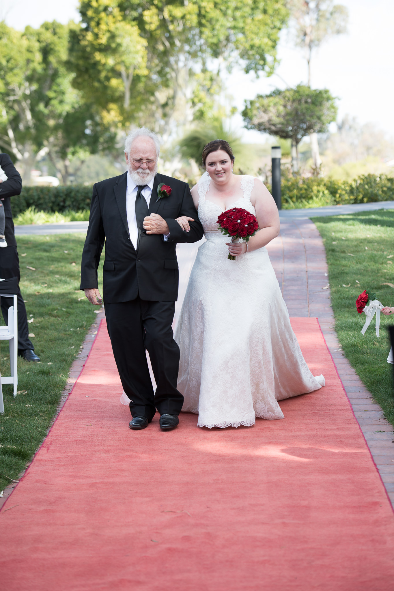 bride walks down the aisle on the red carpet with her father