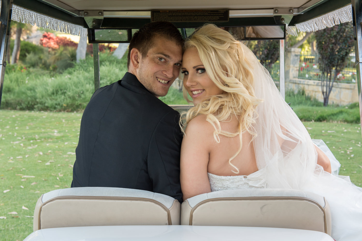 Bride and groom looking over their shoulders on a golf cart