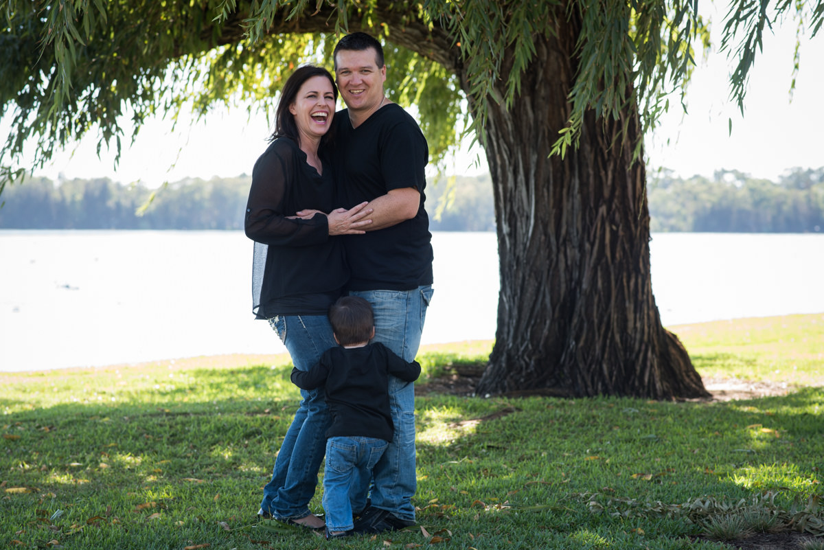 Parents laughing with their little boy hugging their legs by Kruger Photography