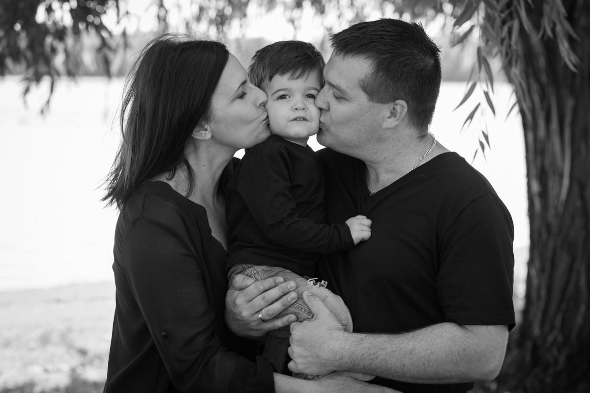 Black and white photo of parents kissing their little boy's cheeks