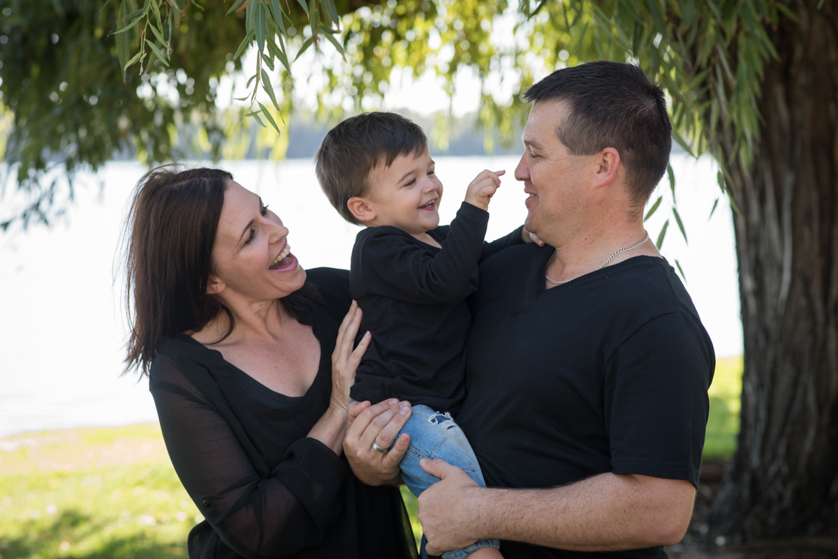 Little point points to his daddy's nose while his mother looks on and smiles