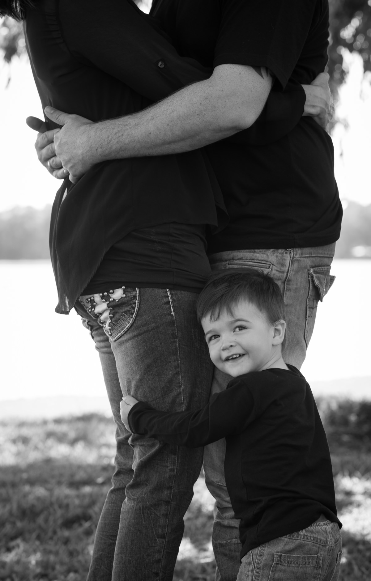 Black and white close up of little boy hugging his parents legs