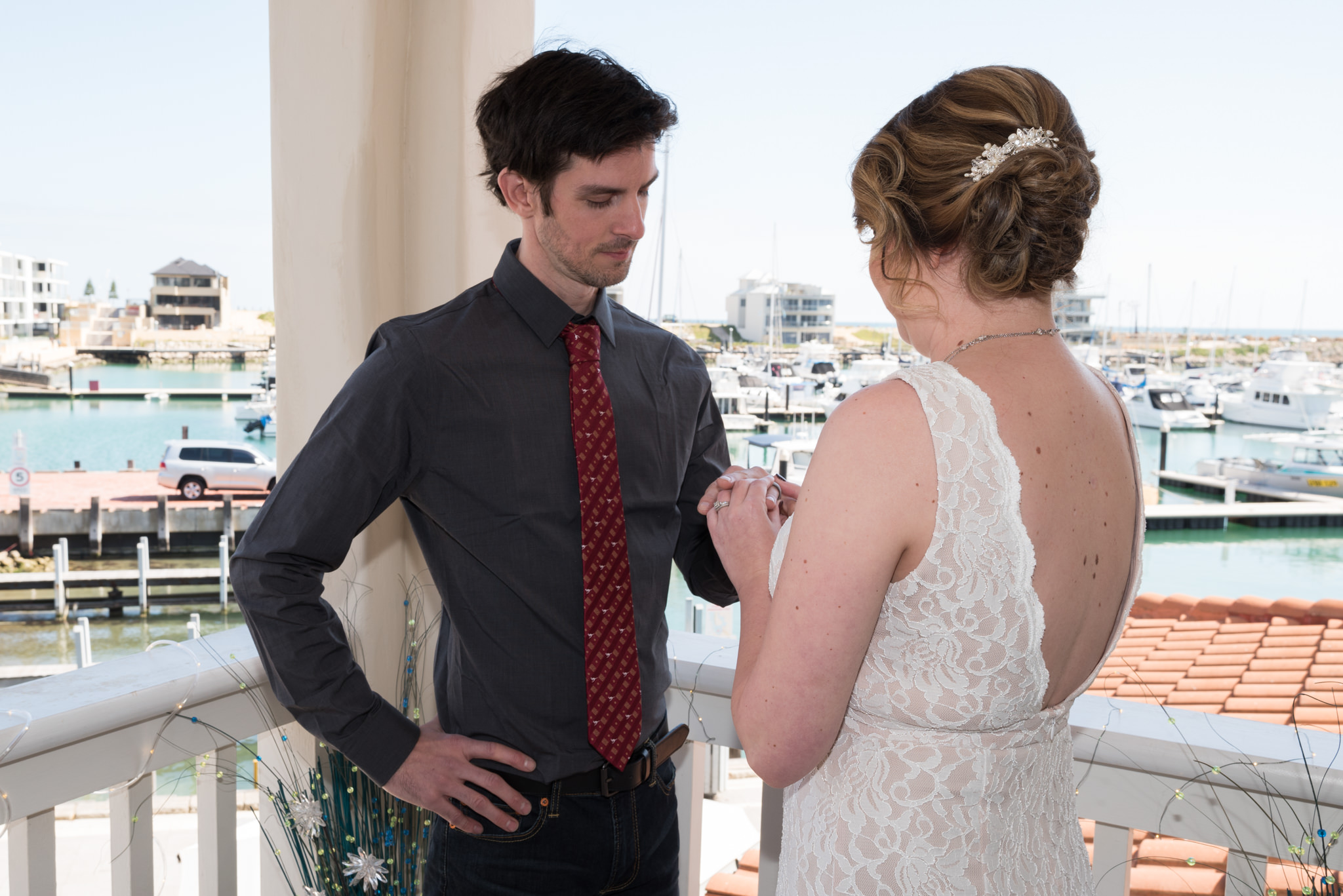 Bride puts the ring on the groom's hand during ceremony on the balcony of their villa at Mindarie Marina