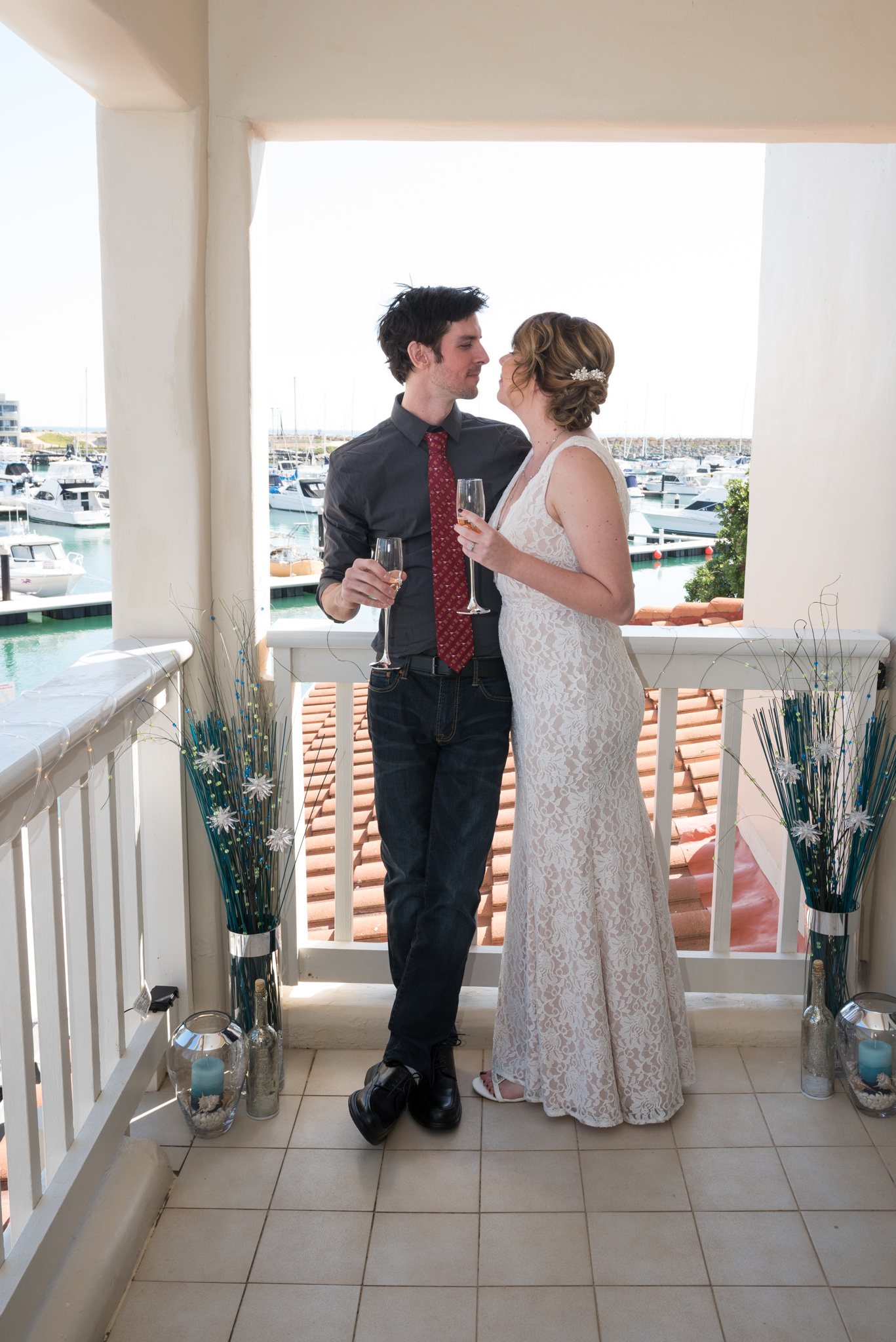 Bride and groom holding champagne glasses on the balcony of their villa at Mindarie Marina