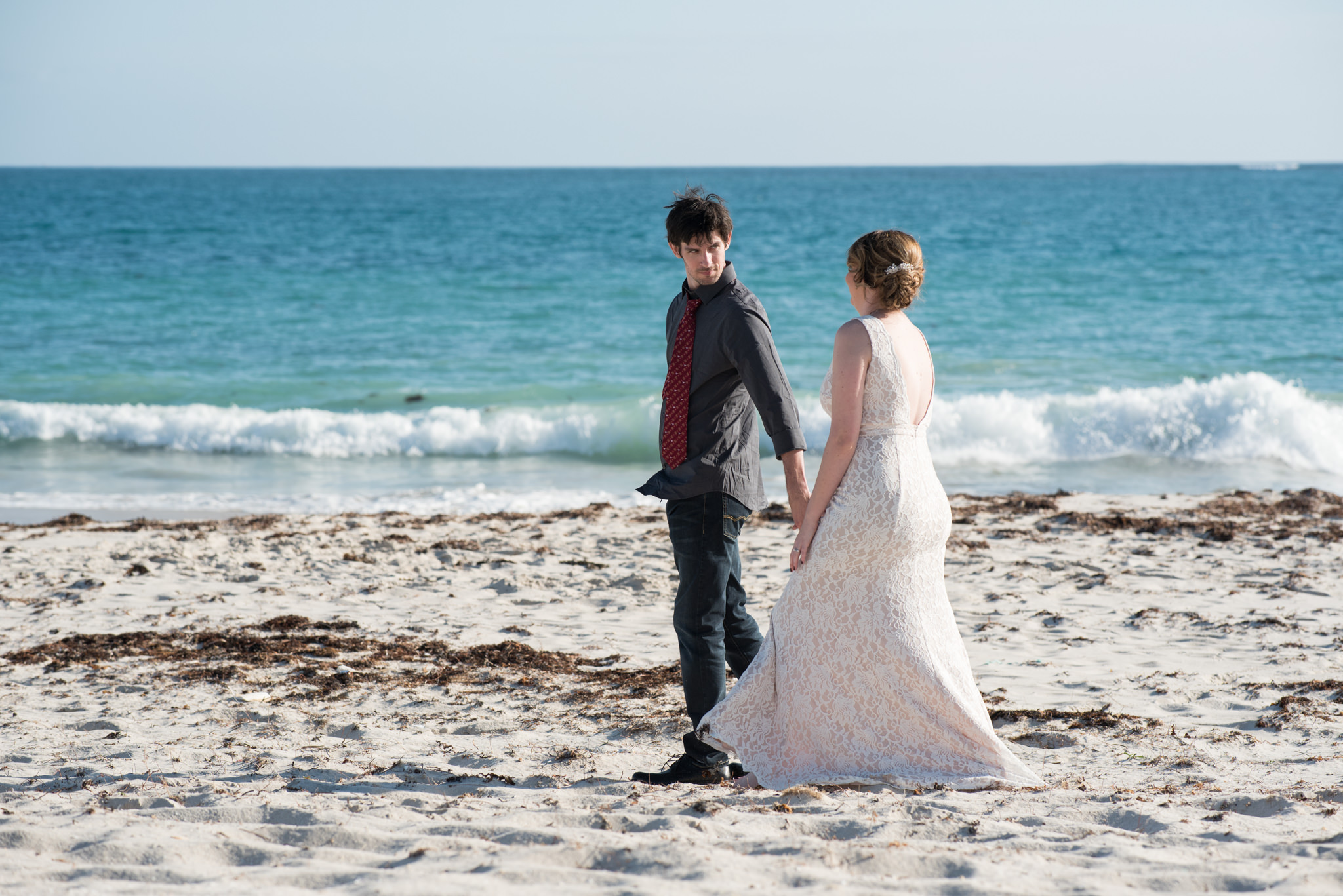 Bride and groom walking along Mindarie beach holding hands