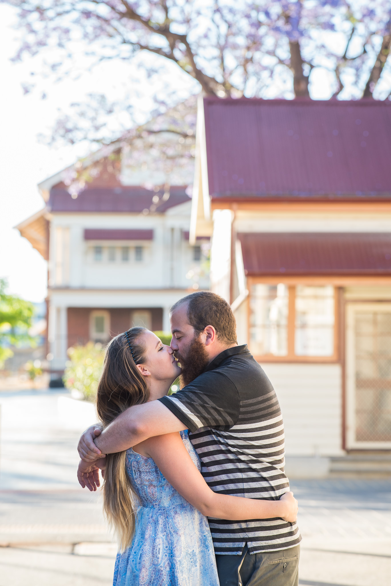 engaged couple cuddling with Jacarandah behind