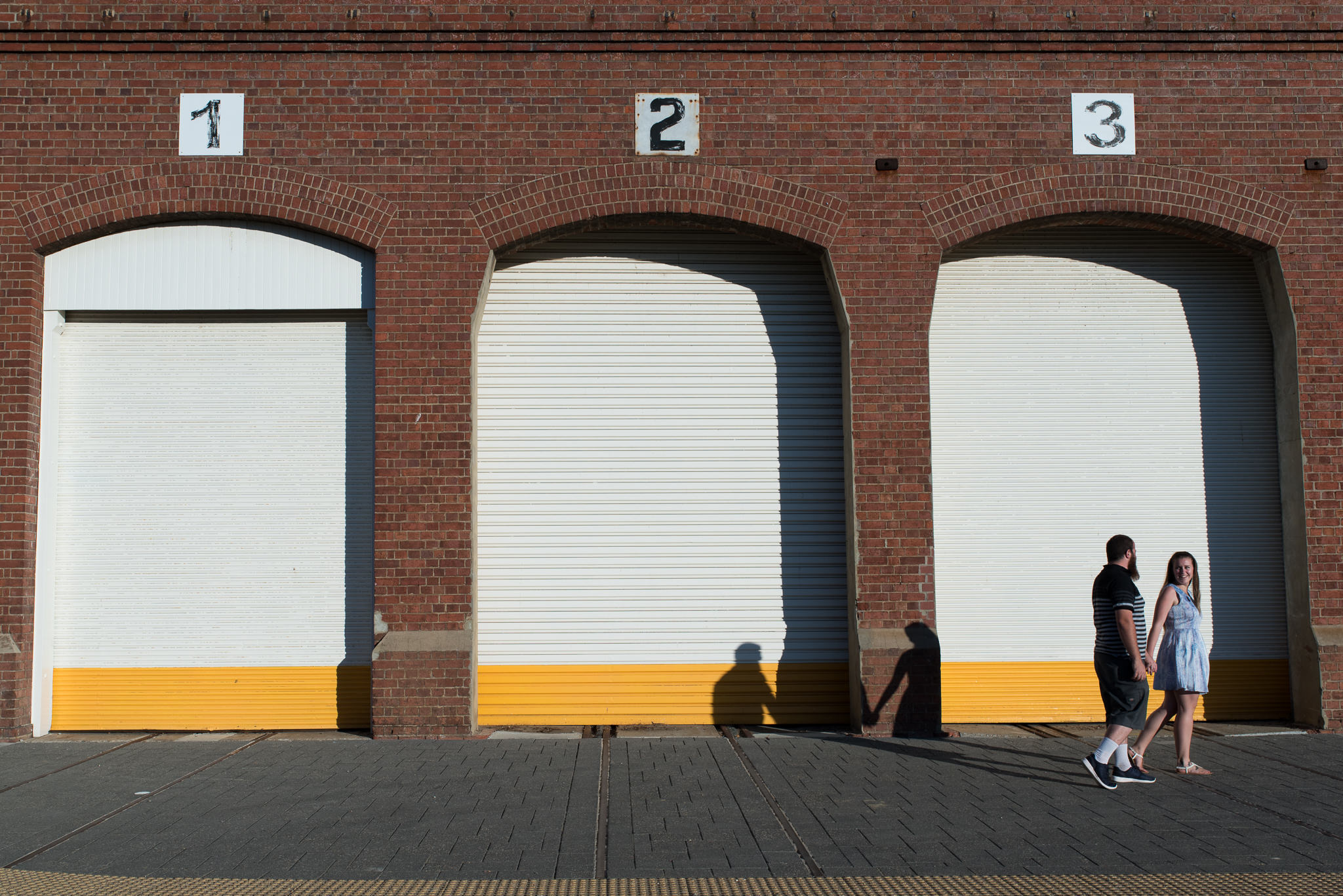 young couple walking along three industrial shed doors