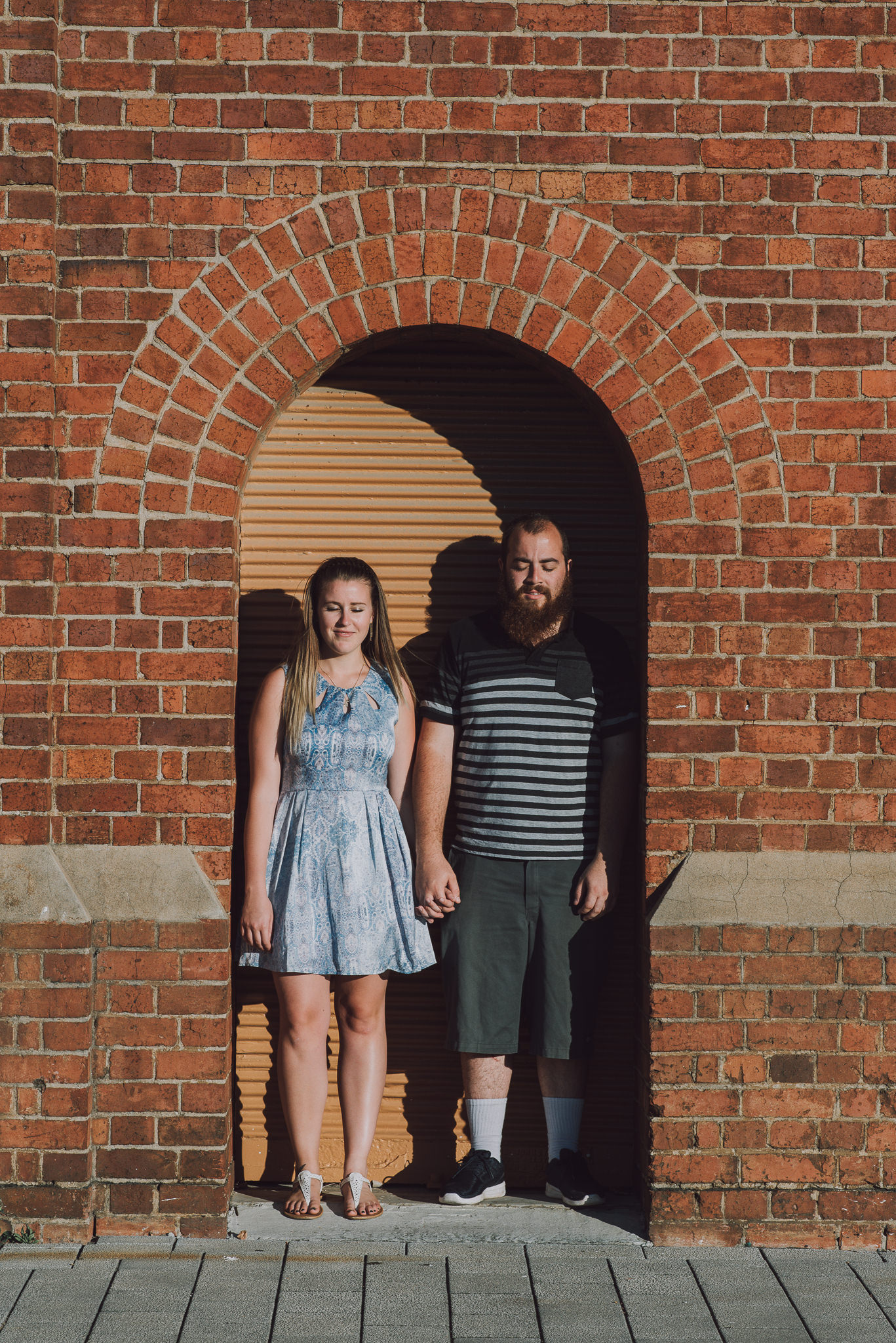 young engaged couple standing in small brick archway with eyes closed