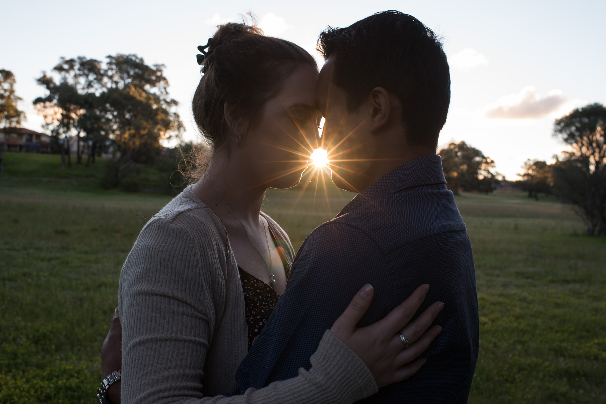 couple holding each other close with late afternoon sun starburst between them