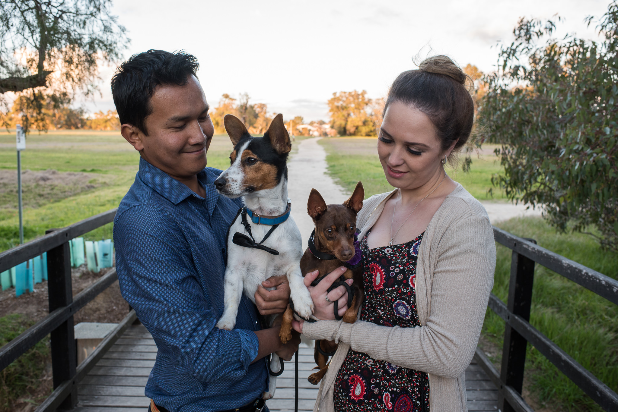 couple cuddling their two dogs in their arms on a bridge