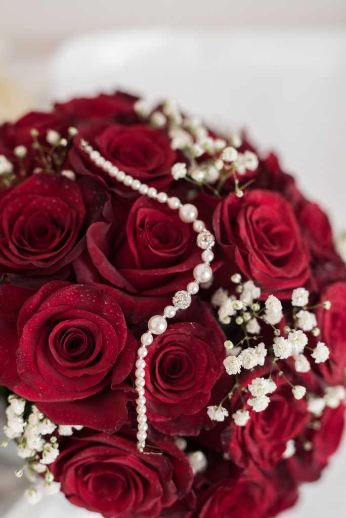 closeup of bridal jewellery on red rose bouquet