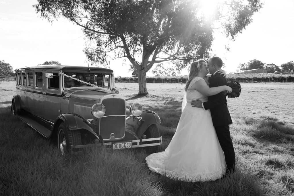 bride and groom hugging in the bush with heir vintage wedding car