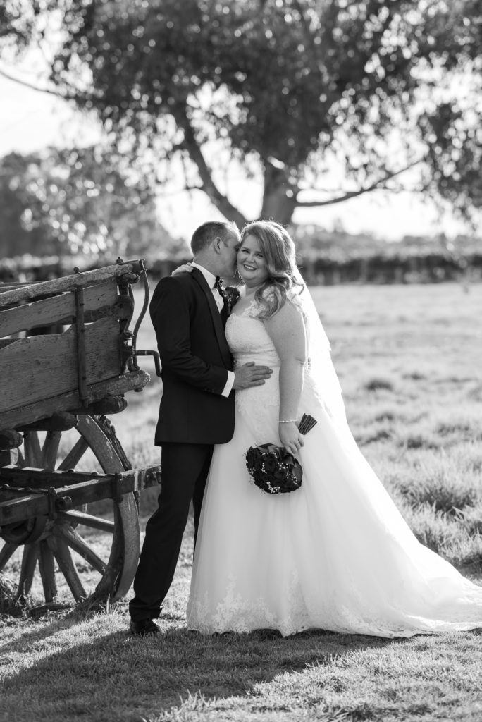 bride and groom cuddling near old wooden wagon