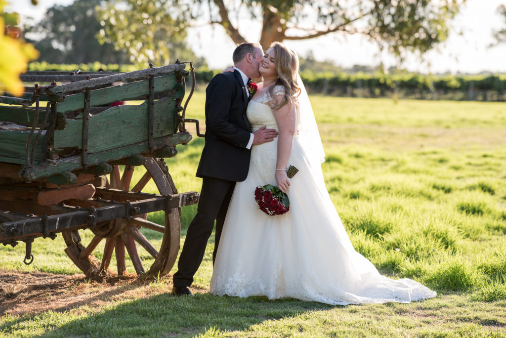 Groom nuzzling bride's neck next to old wagon at Mulberry Estate