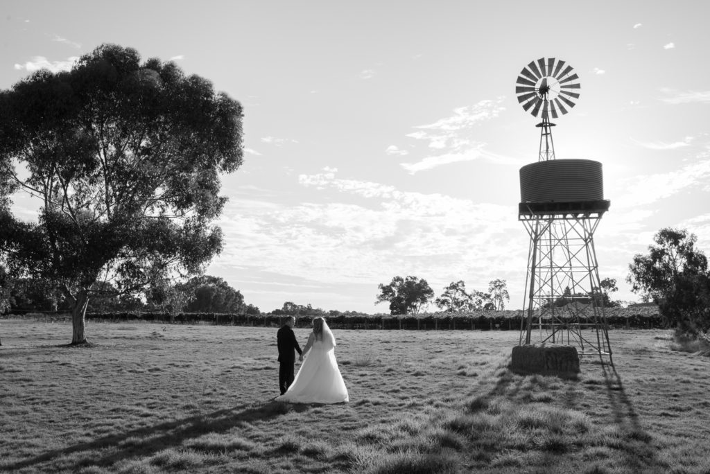 bride and groom holding hands with the windmill and water tank at Mulberry Estate