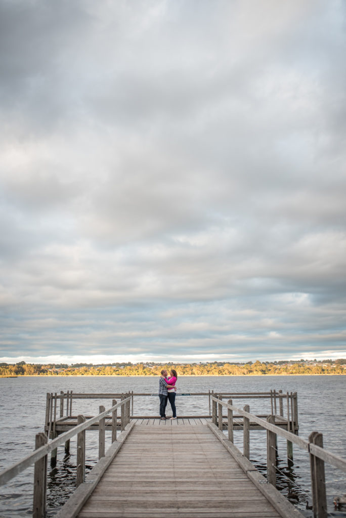 Engaged couple holding each other on the jetty at Neil Hawkins park