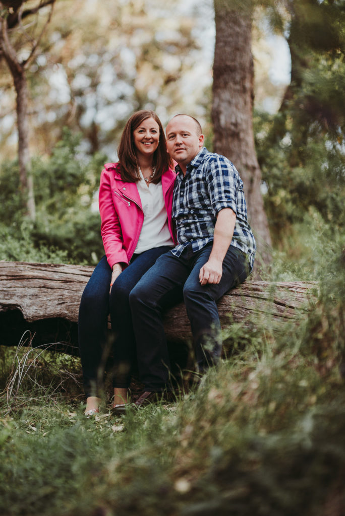 engaged couple sitting on a log in the bush