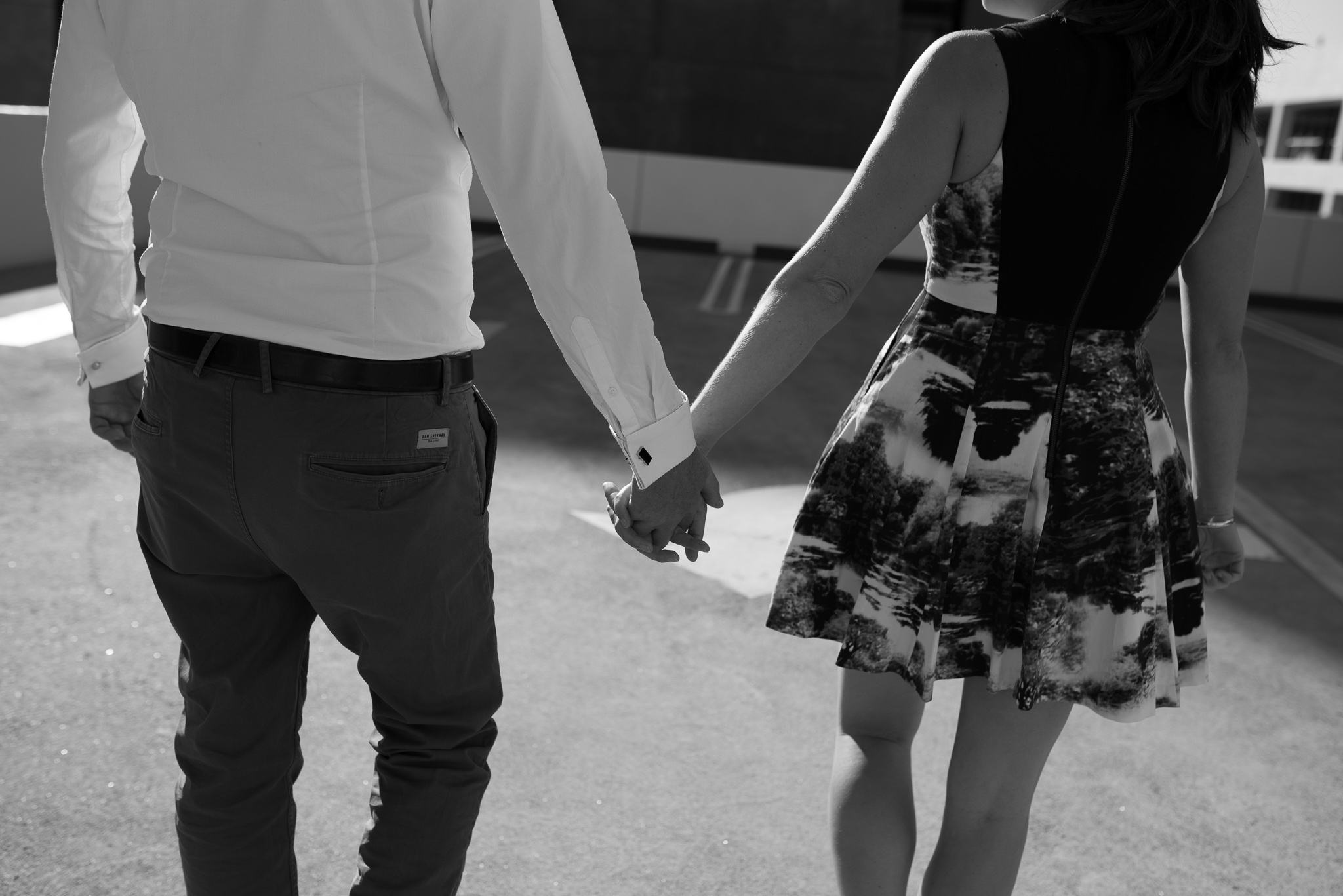 Very low key B&W engaged couple's hands holding on carpark rooftop