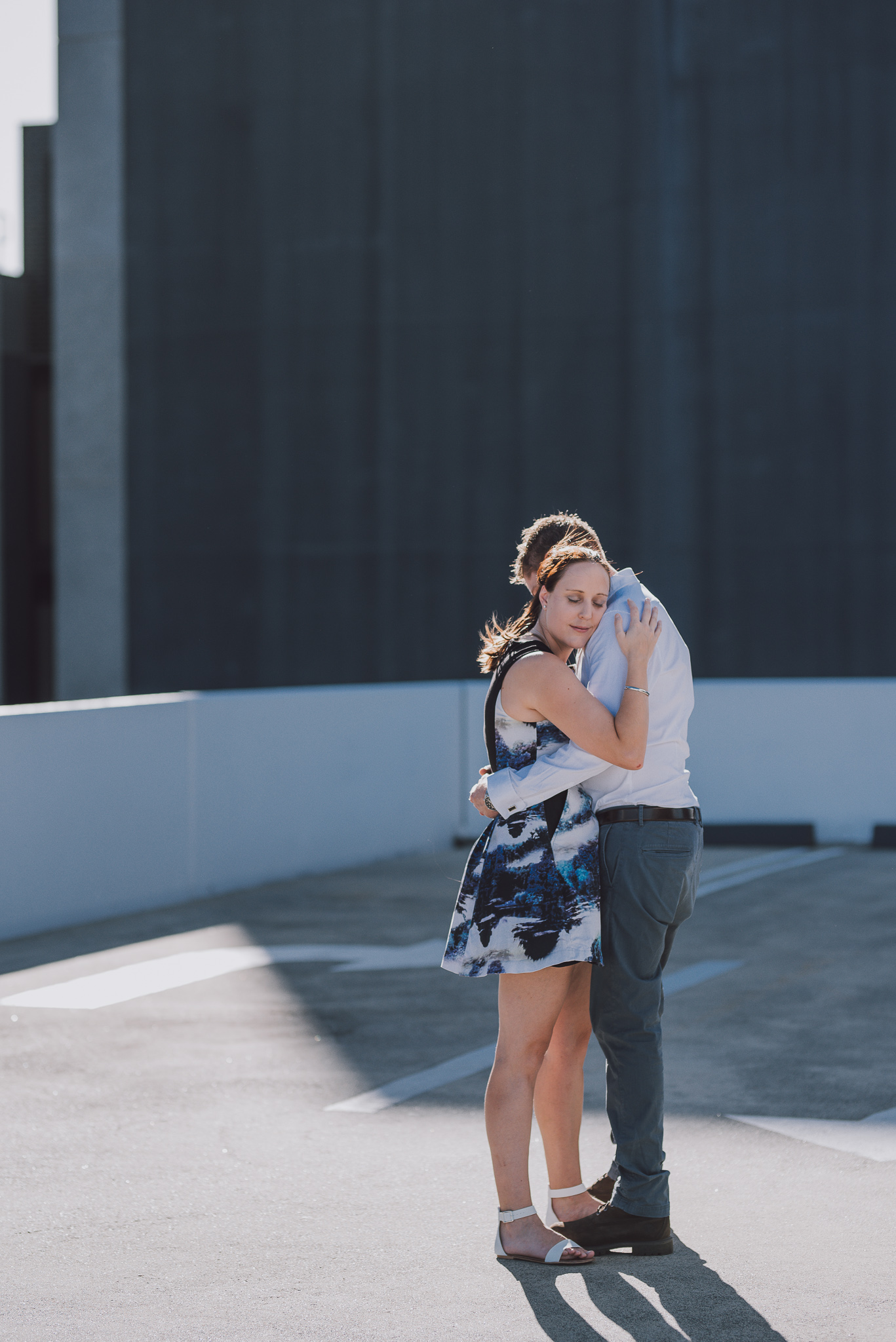 Girl hugs her fiancee with eyes closed during their carpark rooftop engagement shoot