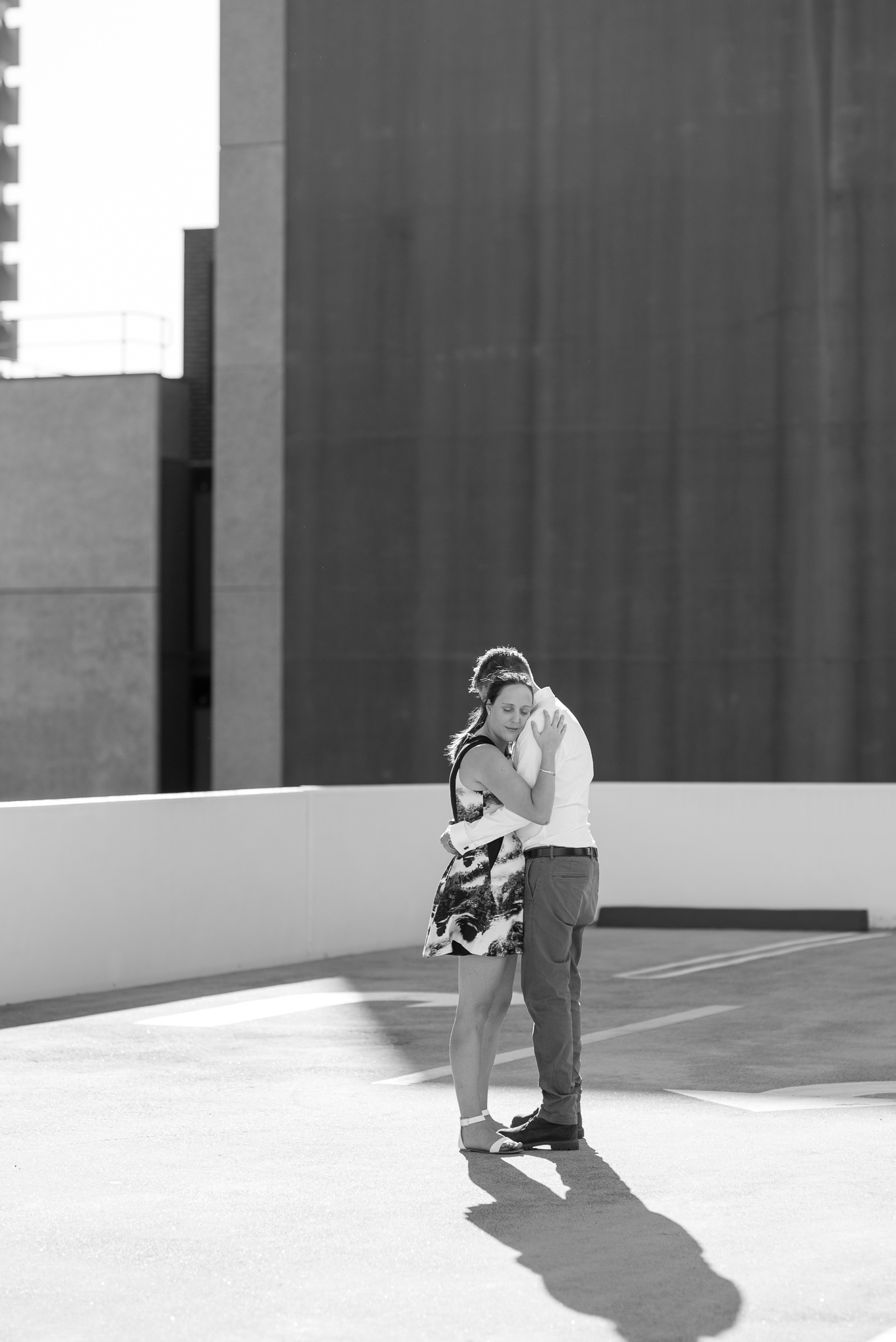 Girl hugs her fiancee during their carpark rooftop engagement shoot