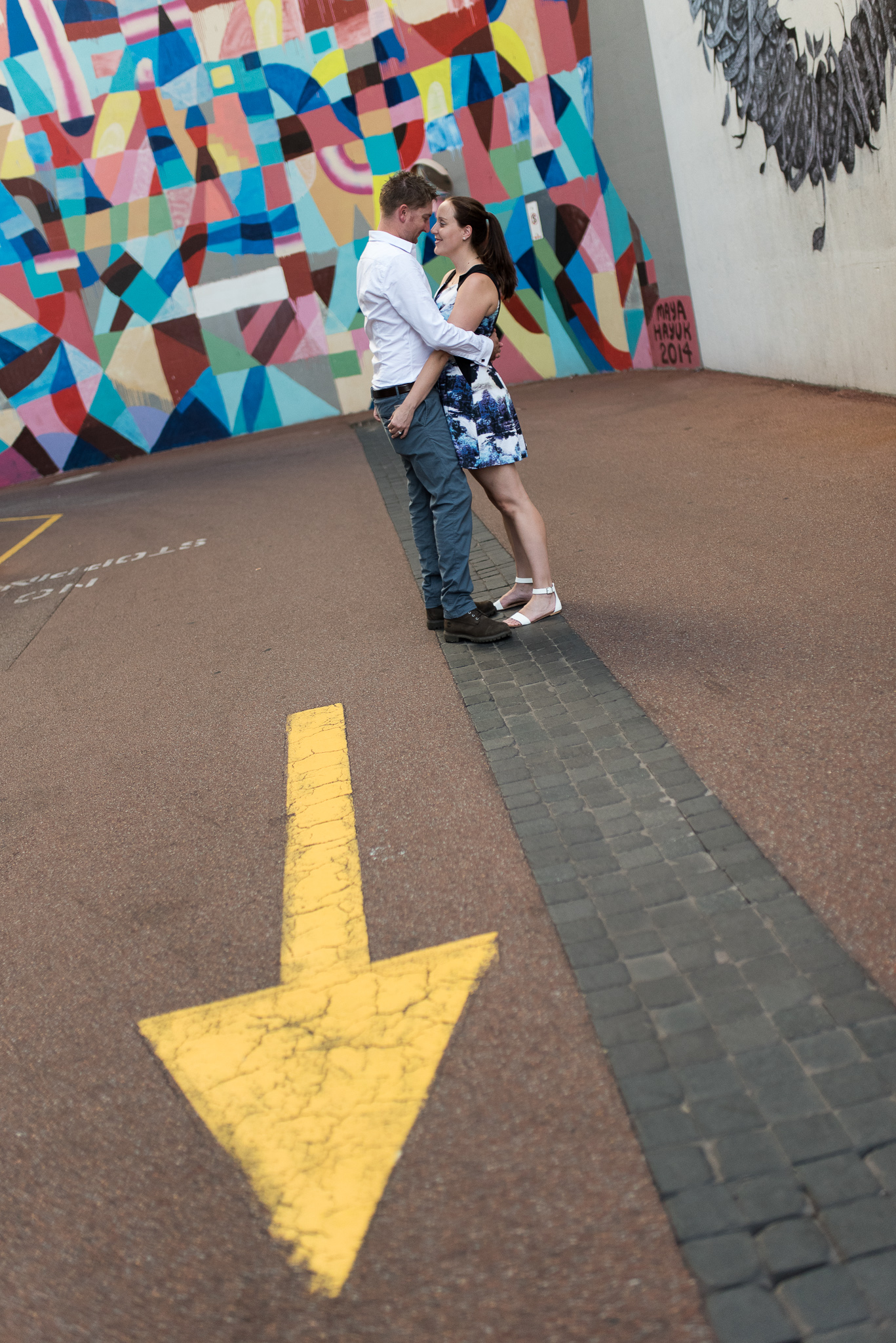 Engaged couple at Wolf Lane with Maya Hayuk mural behind and yellow arrow