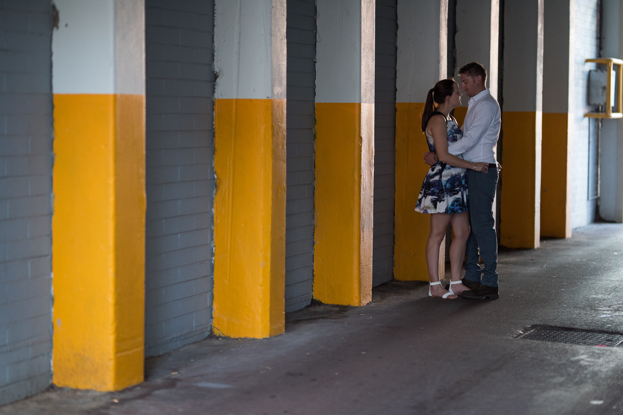 Engaged couple cuddling next to yellow pillars