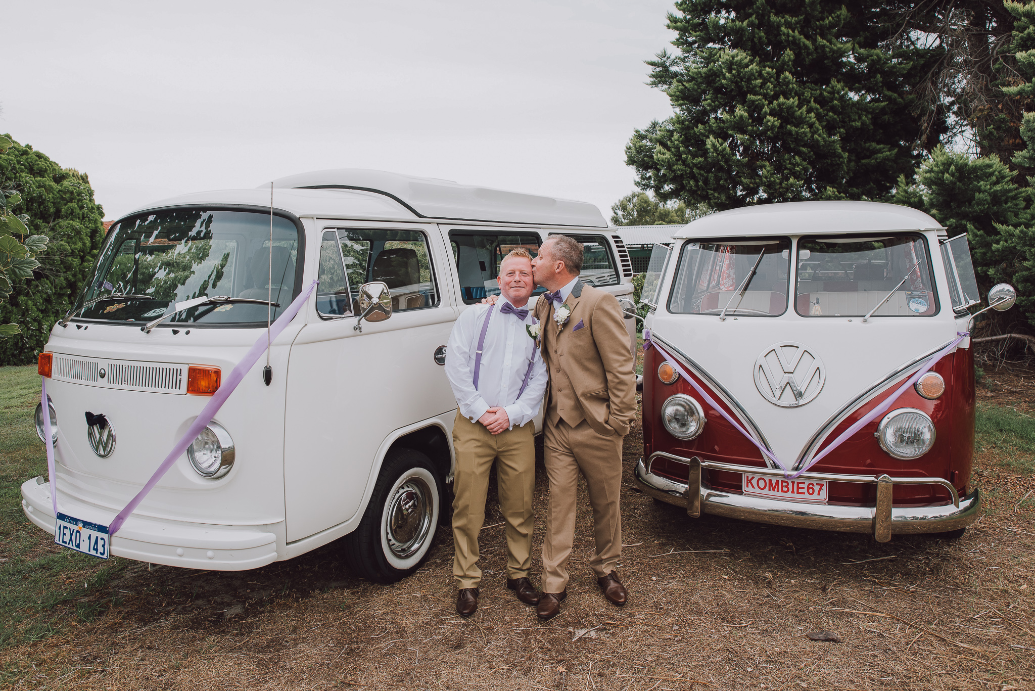 Groom kisses his best man's cheek in between their two vintage kombi vans