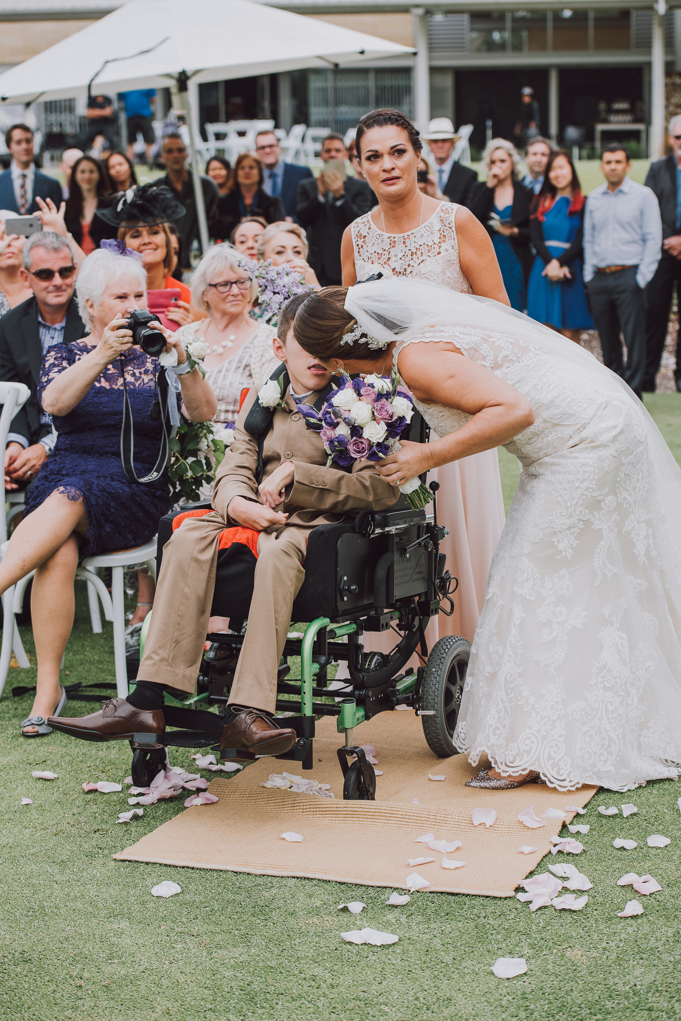 bride kisses her son in a wheelchair after walking her down the aisle