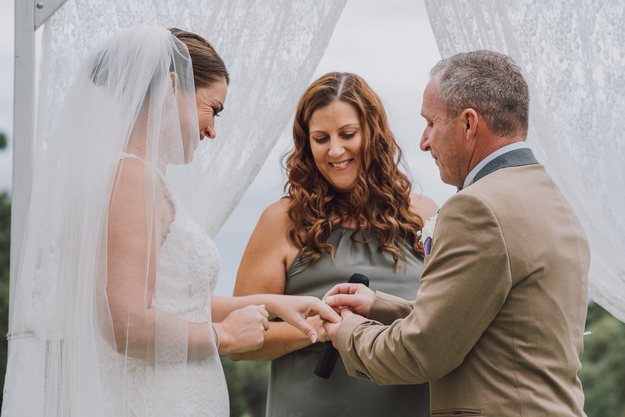 groom puts ring on brides finger with celebrant looking on