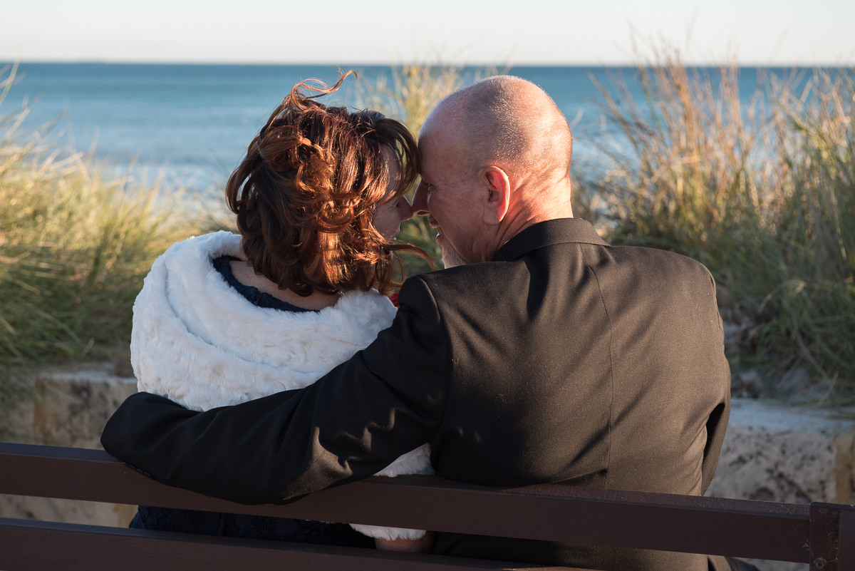 Older wedding couple sitting near ocean with their heads together