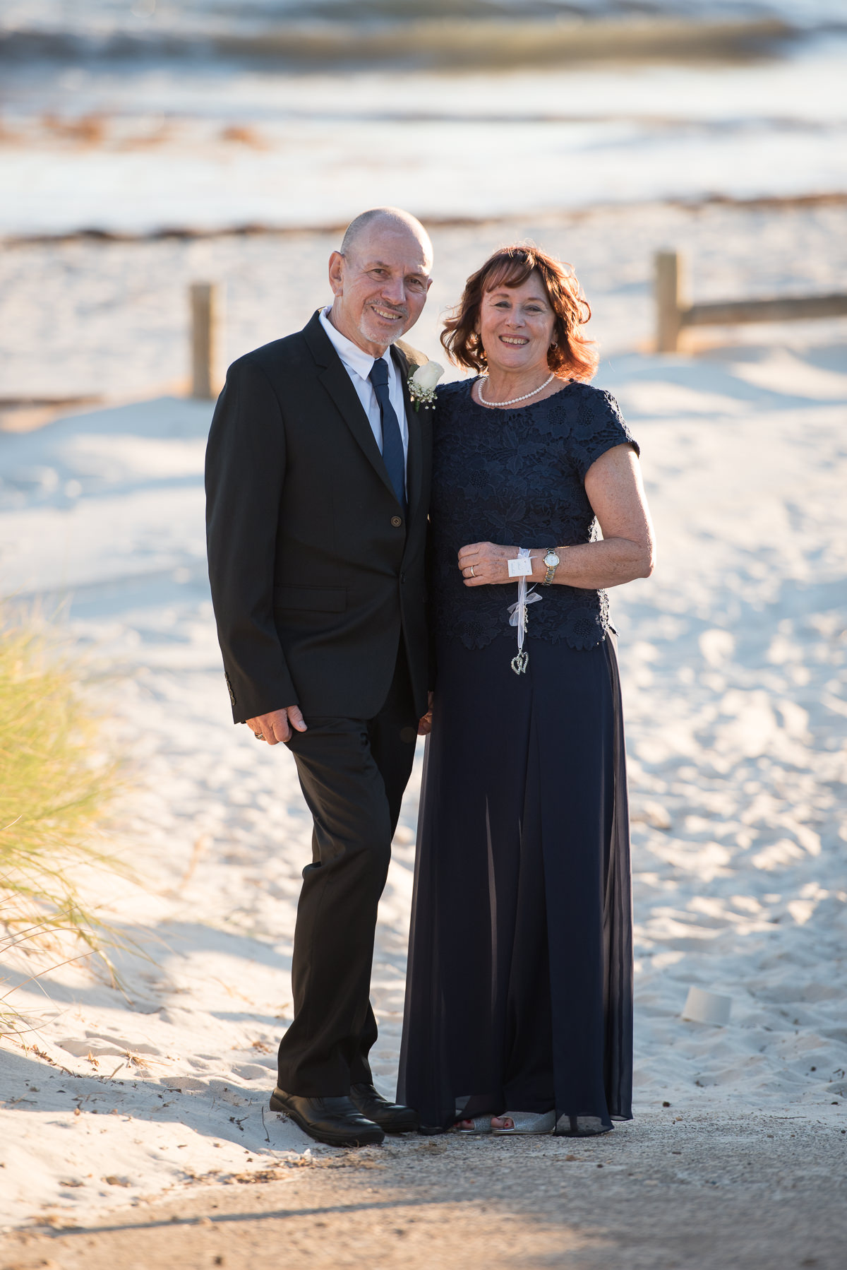 Full length portrait of older wedding couple with beach behind them