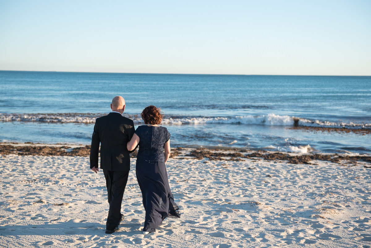 Older wedding couple walking towards the ocean on the beach at Mindarie