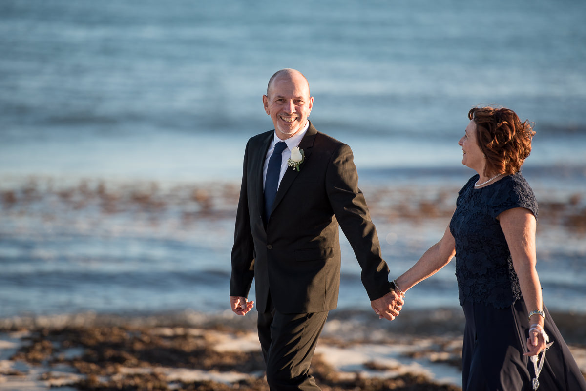 Older groom laughing at camera with bride on the beach