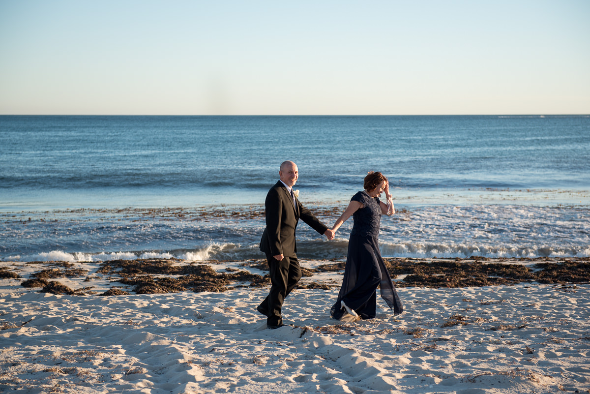 Mature wedding couple walking along beach holding hands