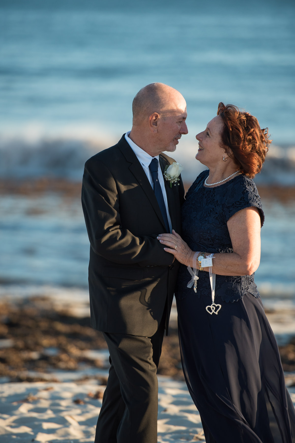 Older wedding couple standing together with the ocean behind them