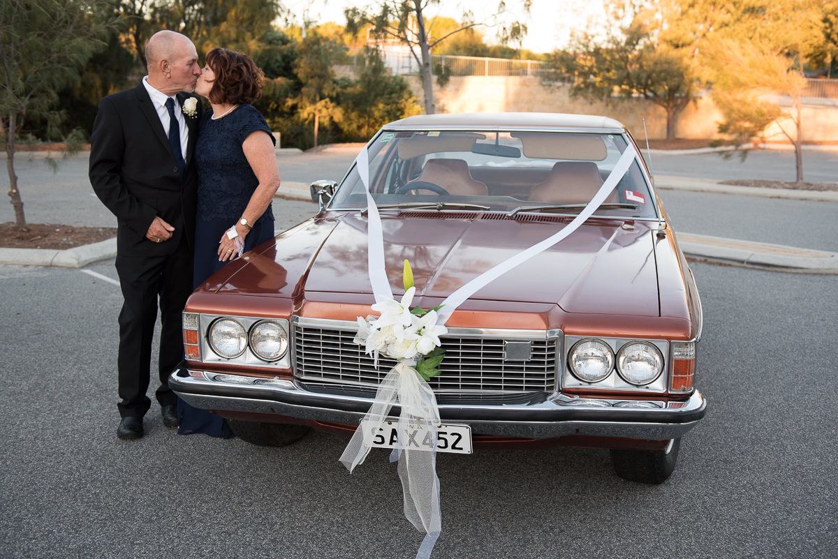 Older wedding couple kissing next to an old Holden premier car