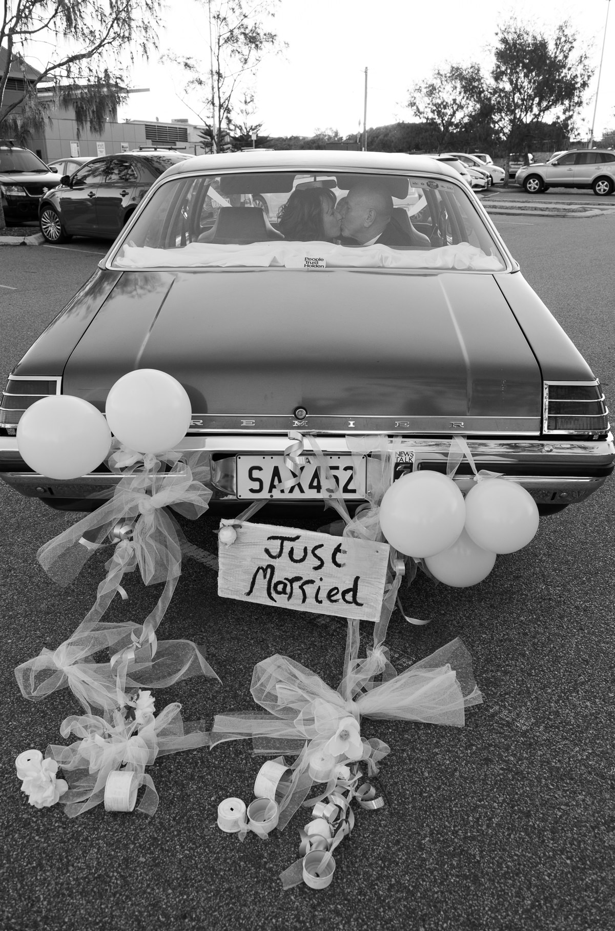 Back of old holden with just married sign and balloons, couple kissing in back seat