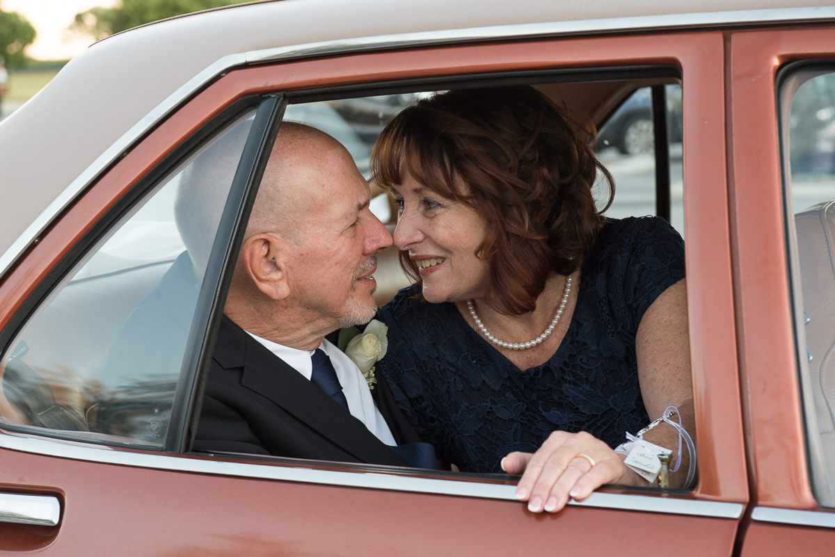 Older wedding couple looking at each other in back seat of car