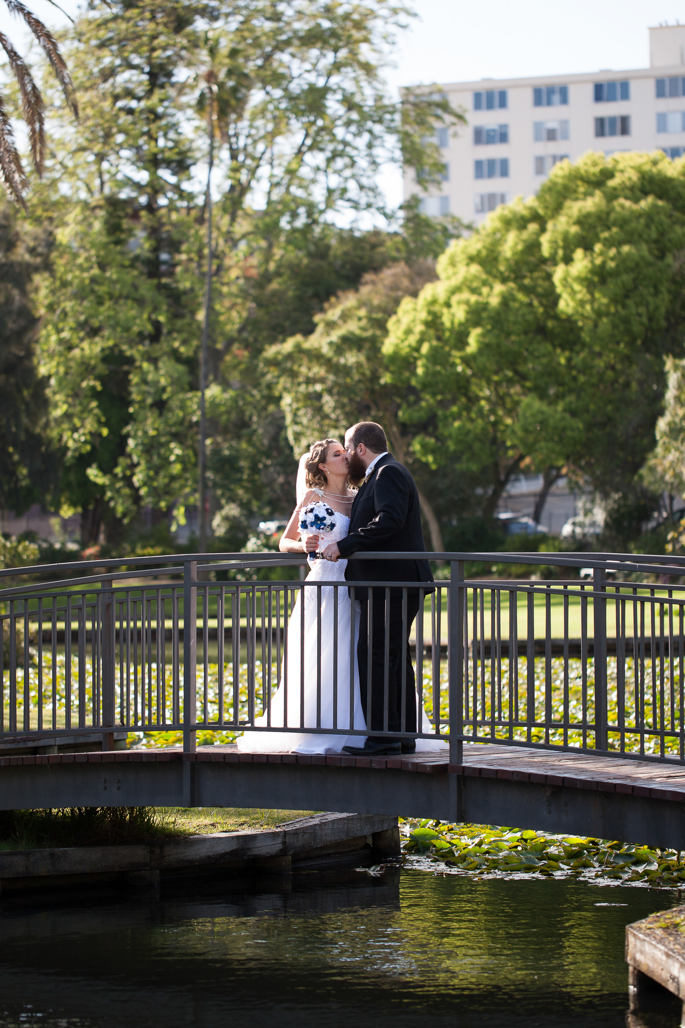 bride and groom standing on a bridge at Queens gardens kissing