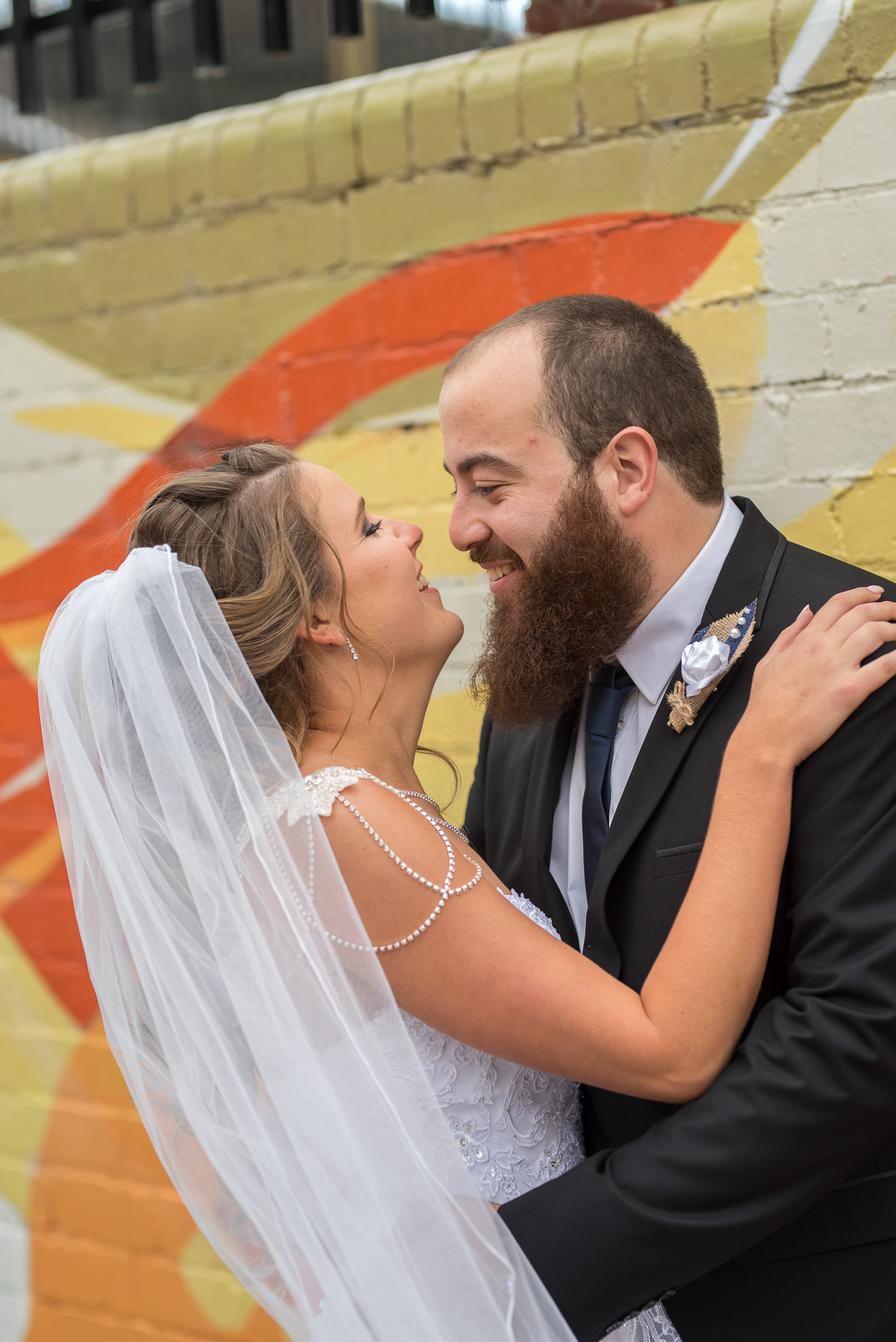 Groom and bride holding each other against painted wall