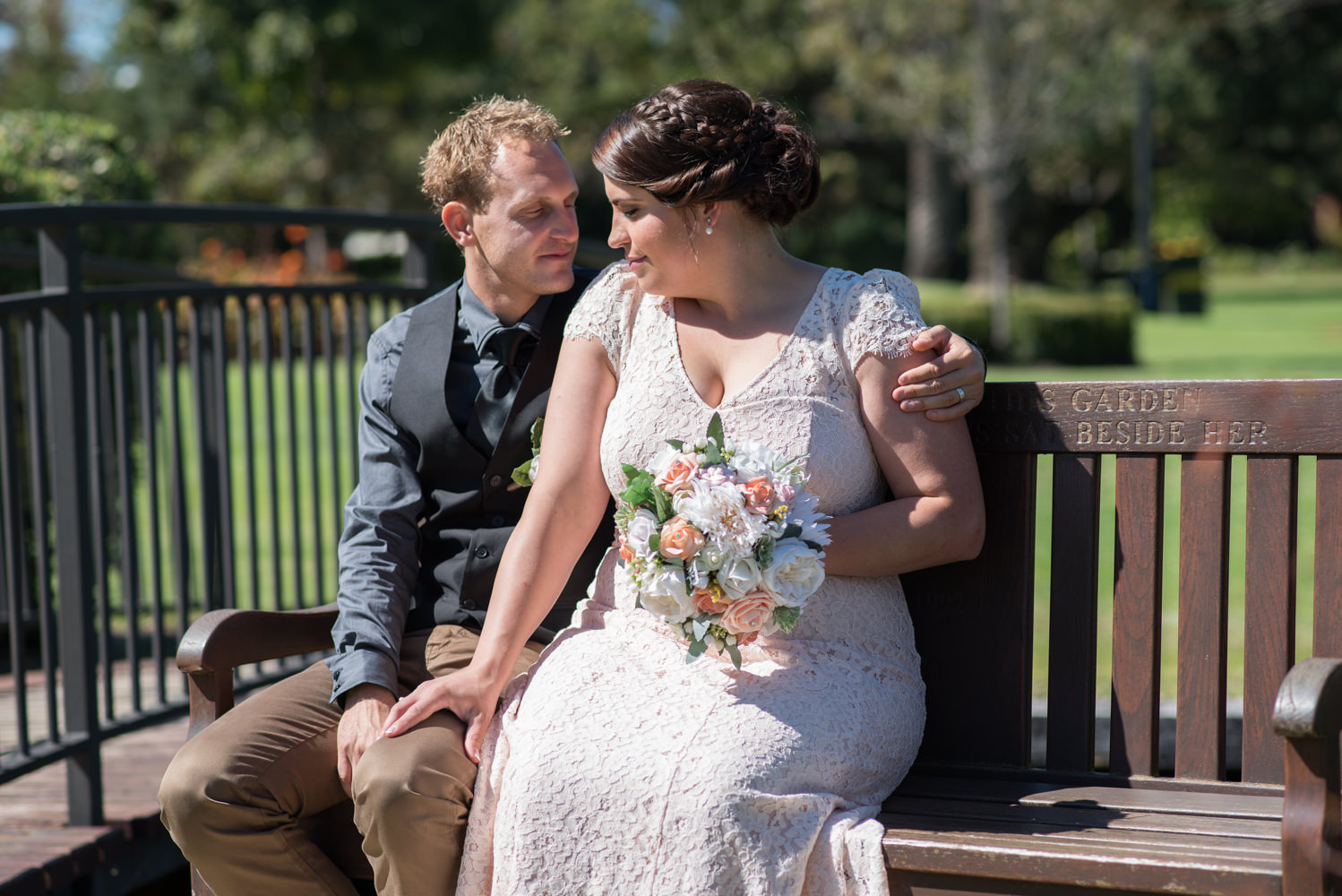 Bride and groom sitting on park seat at Queens gardens