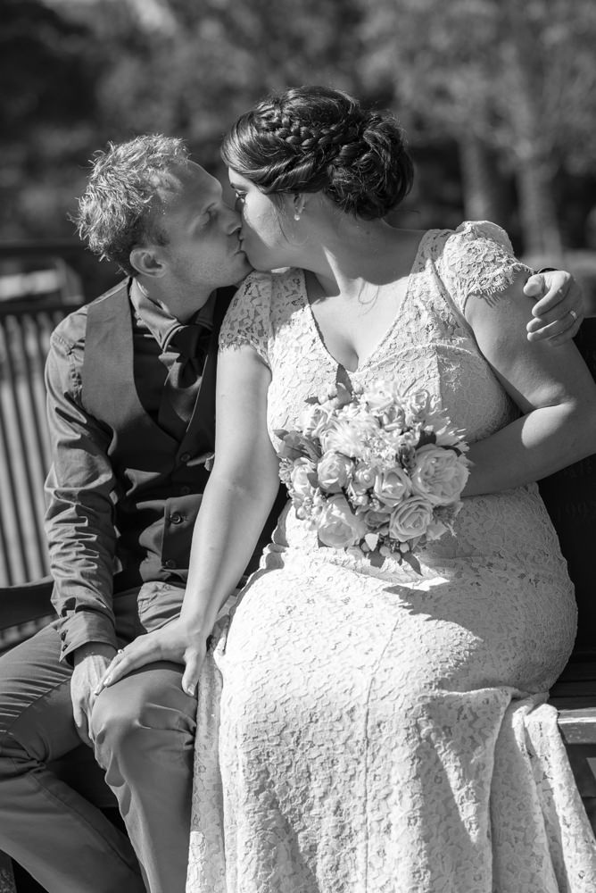 Bride and groom sitting on park seat at Queens gardens