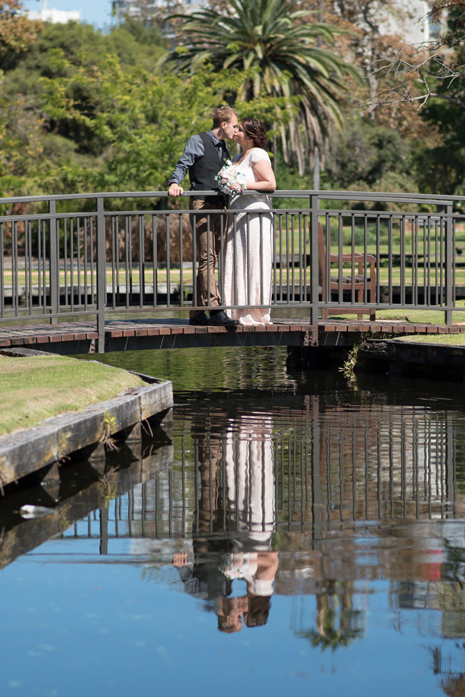 Bride and groom on bridge with reflection at Queens gardens