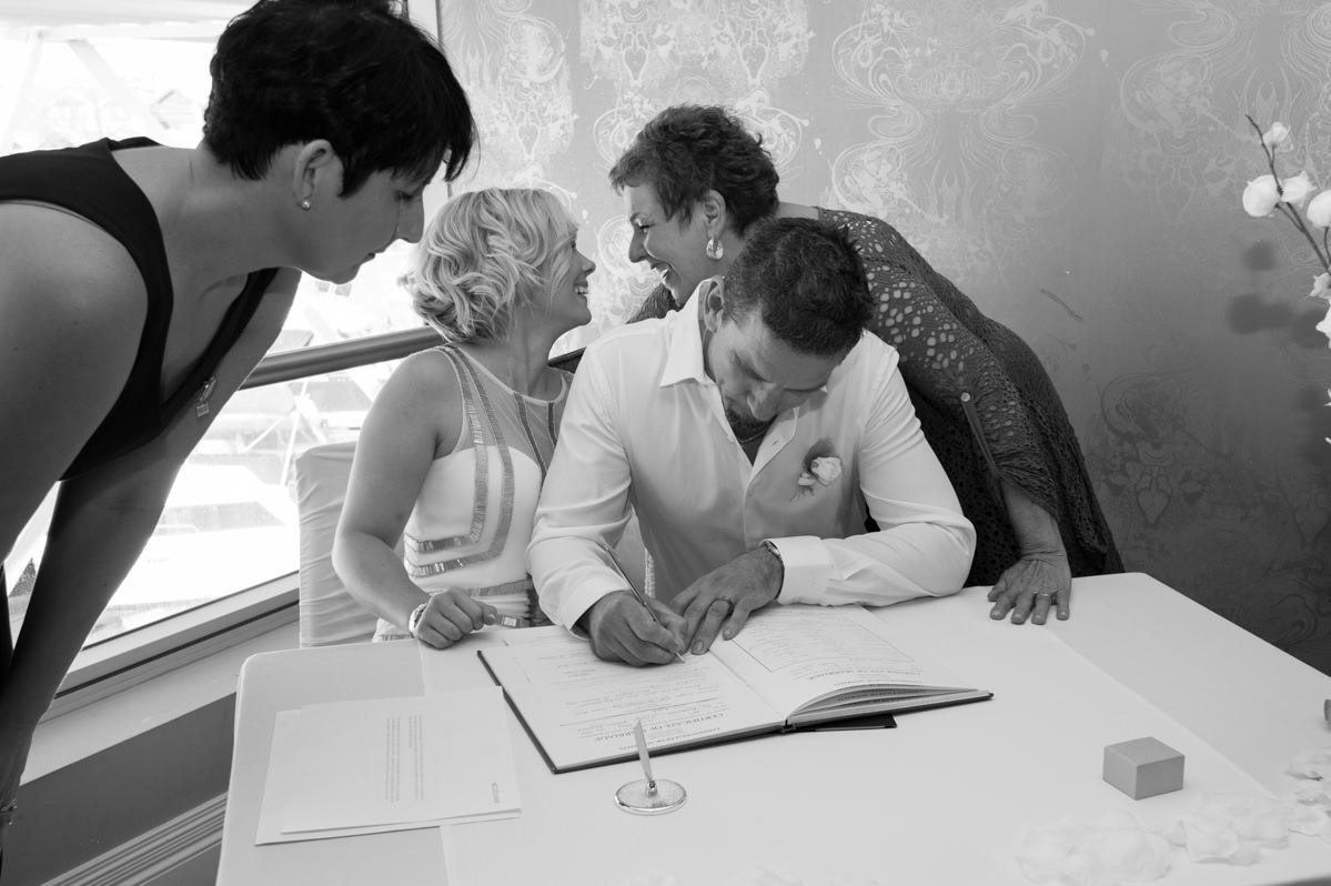 Grooms signs the documents while bride and mother in law smile