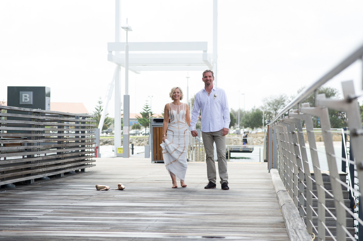 Bride takes her shoes off about to skip on The Breakwater bridge