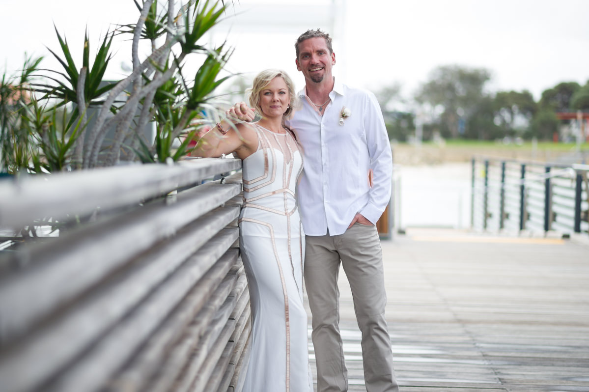 Bride and groom against a fence at The Breakwater